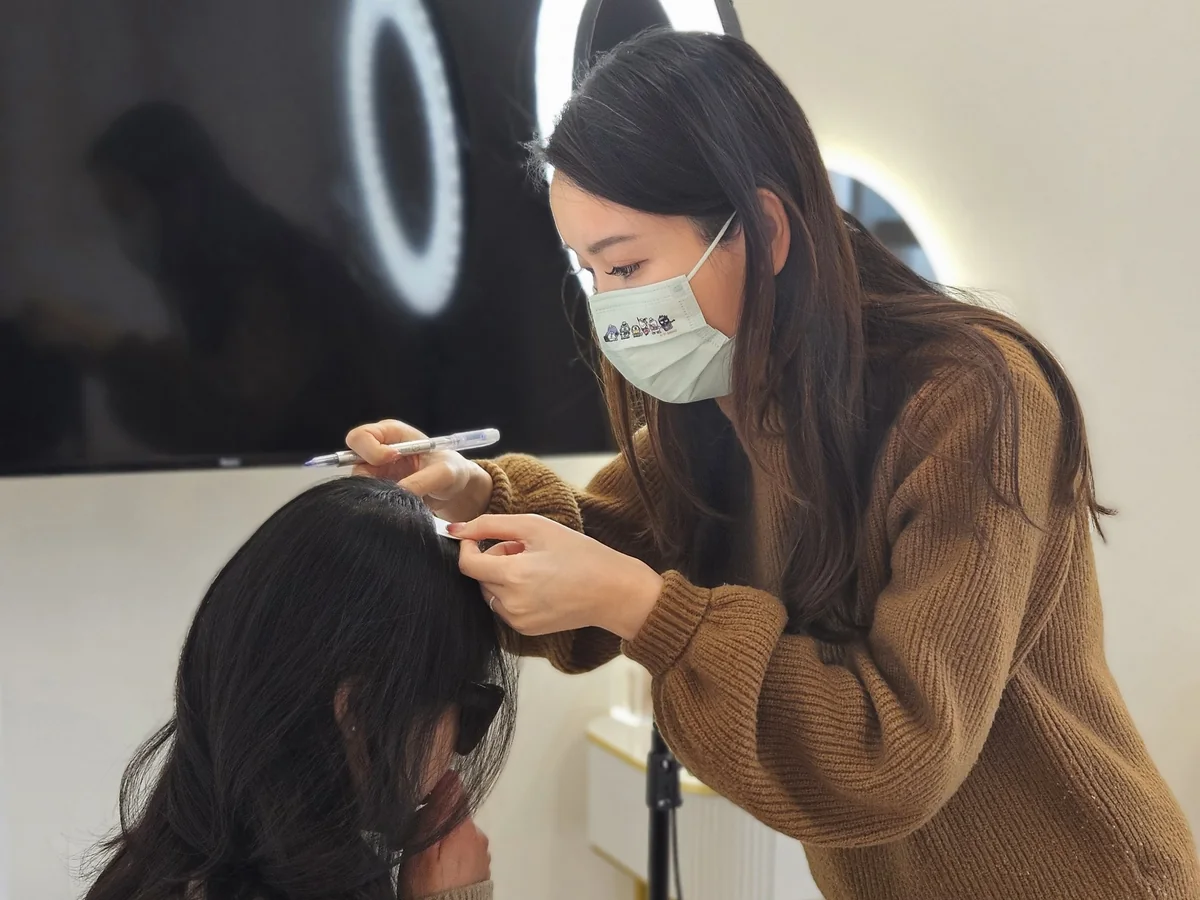 An artist drawing the design line on a client's scalp